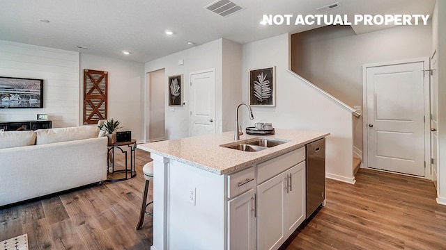 kitchen featuring stainless steel dishwasher, visible vents, a sink, open floor plan, and wood finished floors