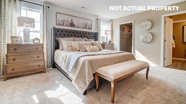bedroom with light colored carpet, a walk in closet, visible vents, and multiple windows