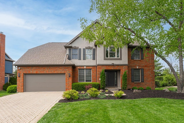 view of front of home with an attached garage, decorative driveway, a front lawn, brick siding, and stucco siding