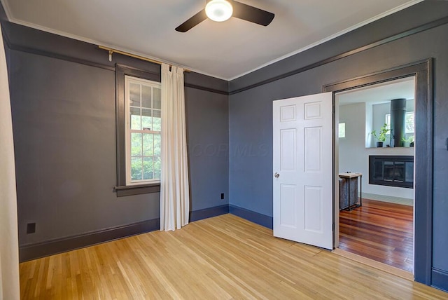 668 Enfield Rd, Columbus, OH 43209 - empty room with light wood-style flooring, crown molding, a glass covered fireplace, ceiling fan, and baseboards