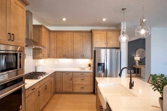 kitchen featuring light countertops, light wood-style flooring, a sink, stainless steel appliances, and wall chimney range hood