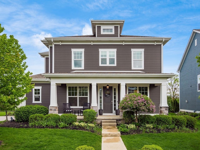 american foursquare style home with a front lawn, stone siding, and covered porch