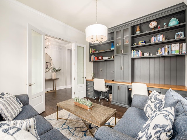 living area featuring dark wood finished floors, crown molding, built in study area, and a notable chandelier