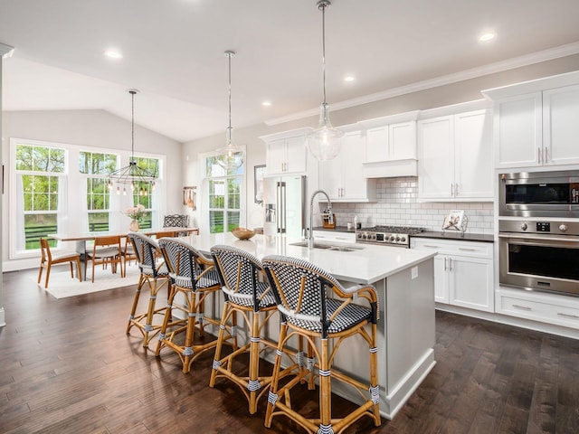 kitchen with a breakfast bar area, a sink, stainless steel appliances, tasteful backsplash, and dark wood-style floors