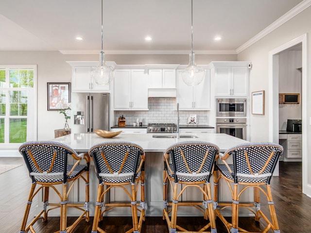 kitchen featuring white cabinetry, decorative backsplash, a center island with sink, and appliances with stainless steel finishes