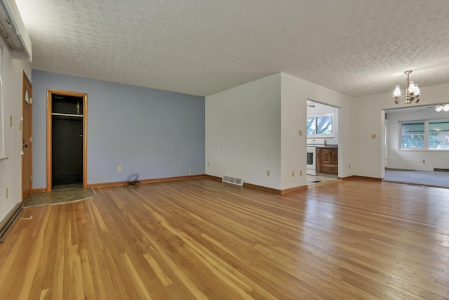 unfurnished living room featuring a textured ceiling, a chandelier, light wood-type flooring, and baseboards
