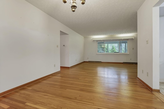 empty room featuring light wood finished floors, a textured ceiling, baseboards, and a chandelier