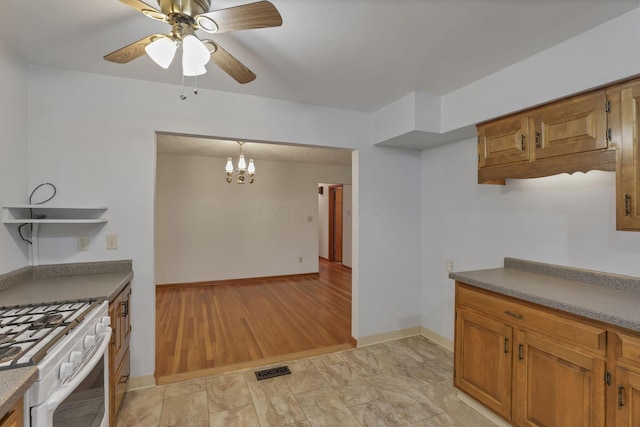 kitchen featuring gas range gas stove, brown cabinetry, a ceiling fan, a chandelier, and baseboards