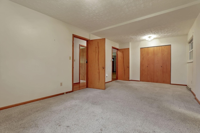 unfurnished bedroom featuring a closet, light carpet, a textured ceiling, and baseboards