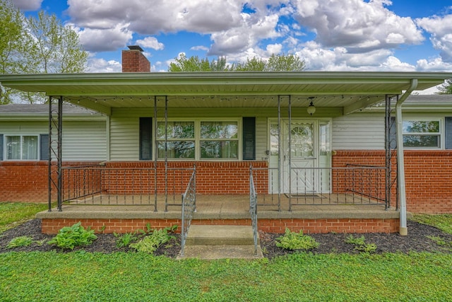 doorway to property featuring covered porch, brick siding, and a chimney