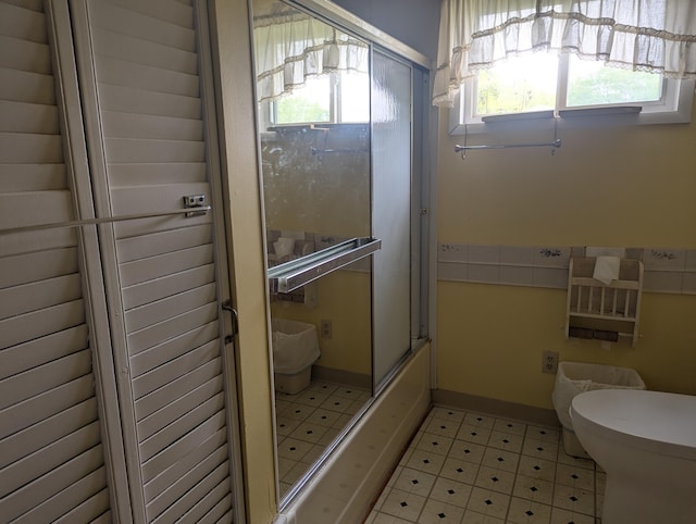 full bath with tile patterned floors, toilet, and shower / bath combination with glass door