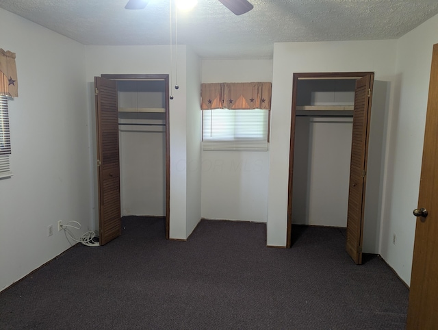 unfurnished bedroom featuring two closets, a ceiling fan, dark carpet, and a textured ceiling