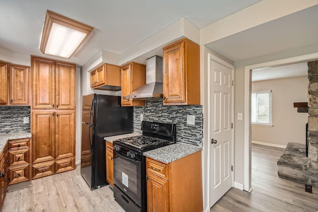 3140 Hamilton Ave, Columbus, OH 43224 - kitchen featuring black appliances, wall chimney exhaust hood, light stone counters, decorative backsplash, and light wood-style floors