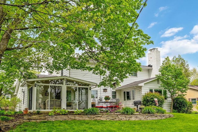 rear view of house featuring a sunroom, a chimney, and a lawn