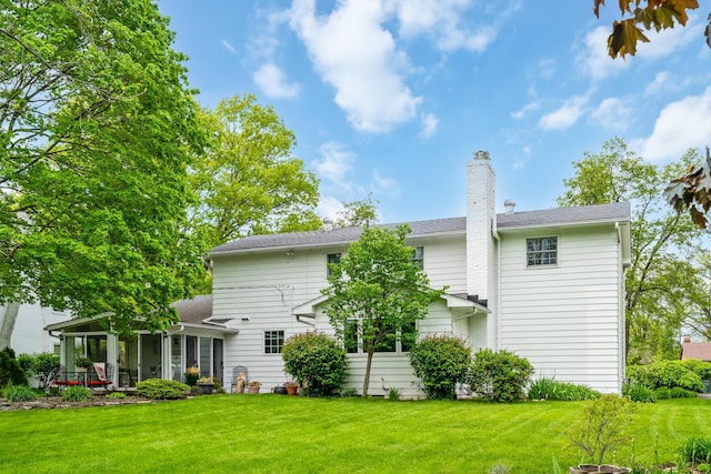 rear view of property with a lawn, a chimney, and a sunroom