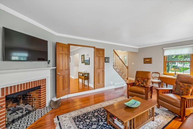 living area with wood finished floors, stairs, ornamental molding, a brick fireplace, and baseboards