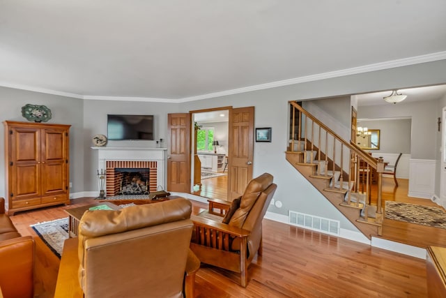 living room featuring stairway, light wood-style flooring, a fireplace, a chandelier, and crown molding