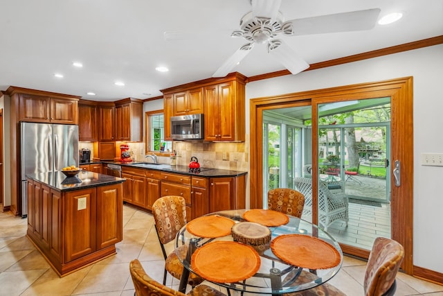 kitchen featuring appliances with stainless steel finishes, a sink, decorative backsplash, ceiling fan, and a kitchen island