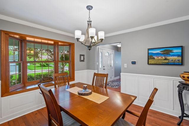 dining room with a chandelier, ornamental molding, wood finished floors, and wainscoting