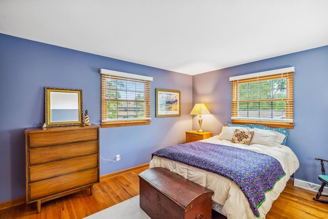 bedroom with multiple windows, wood finished floors, and baseboards