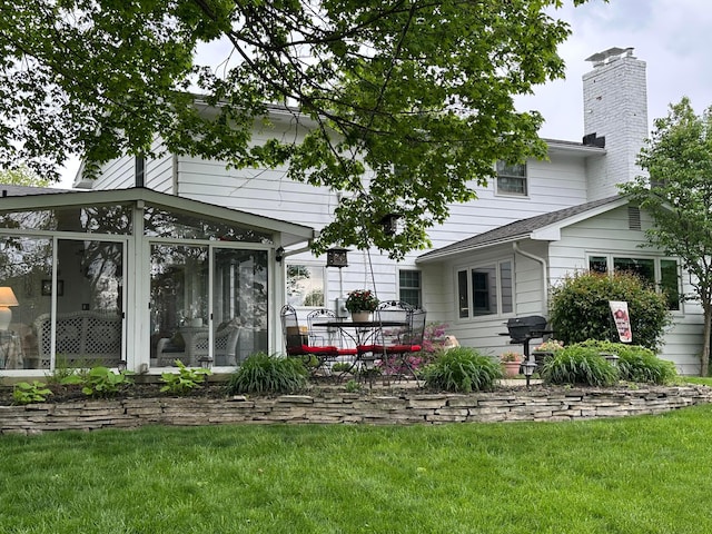 back of property with a sunroom, a chimney, and a lawn