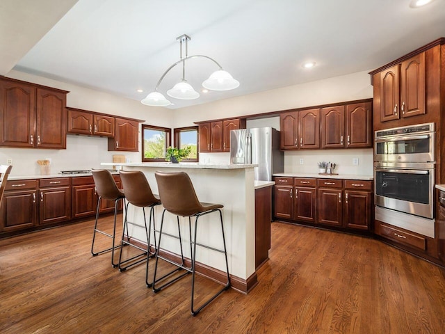 kitchen featuring stainless steel appliances, a center island, dark wood finished floors, a kitchen bar, and light countertops