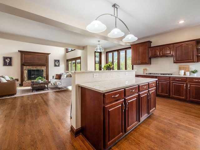kitchen with stainless steel gas cooktop, a brick fireplace, open floor plan, dark wood-style floors, and hanging light fixtures