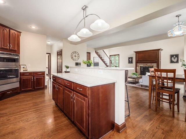 kitchen with pendant lighting, a center island, dark wood finished floors, stainless steel double oven, and a kitchen breakfast bar