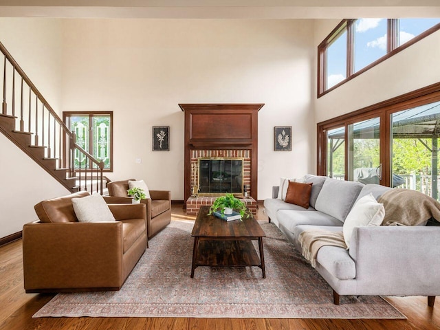 living area featuring wood finished floors, a towering ceiling, a brick fireplace, and stairs