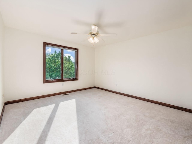empty room with baseboards, visible vents, a ceiling fan, and light colored carpet