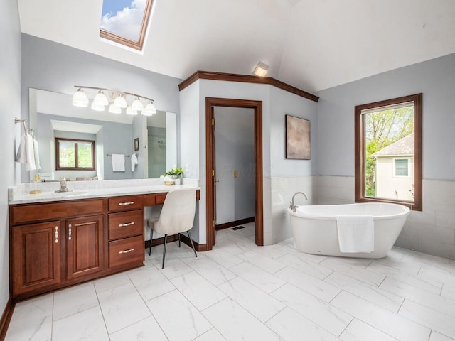 bathroom with vaulted ceiling with skylight, tile walls, a freestanding bath, and a healthy amount of sunlight
