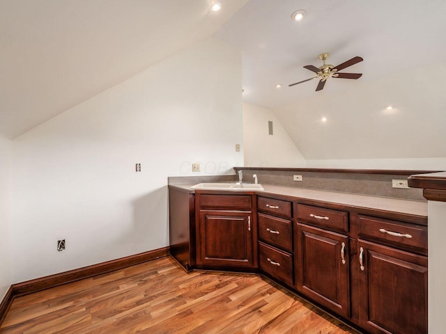 kitchen with baseboards, ceiling fan, a sink, vaulted ceiling, and light wood-style floors