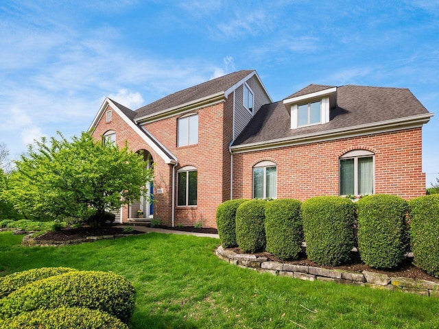 rear view of house featuring a yard, brick siding, and roof with shingles
