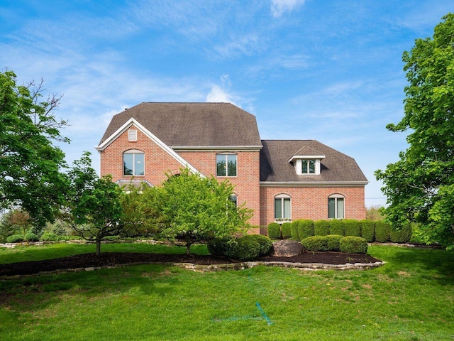 view of front facade with a front yard, roof with shingles, and brick siding