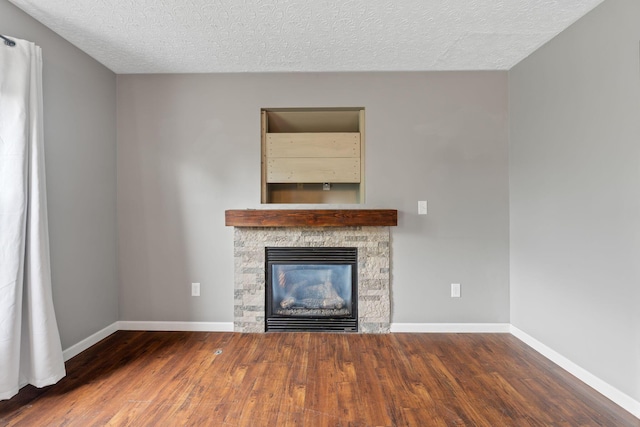 unfurnished living room featuring baseboards, a stone fireplace, a textured ceiling, and wood finished floors