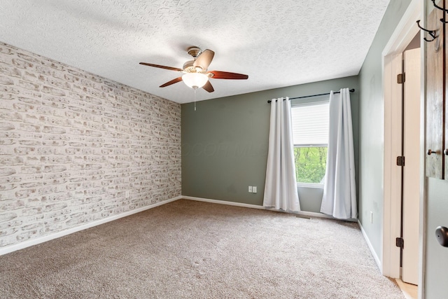 spare room featuring a textured ceiling, carpet flooring, a ceiling fan, brick wall, and baseboards