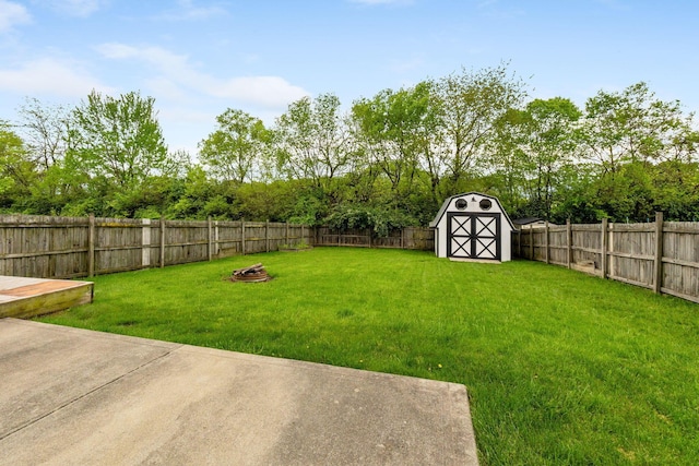 view of yard featuring a storage unit, a fenced backyard, a fire pit, and an outbuilding