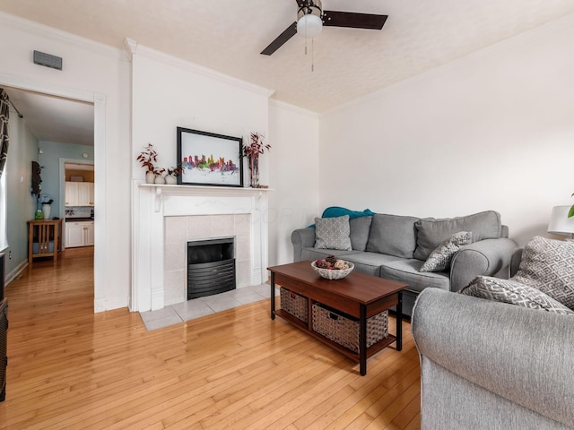 living area with ornamental molding, a tile fireplace, ceiling fan, and light wood-style floors