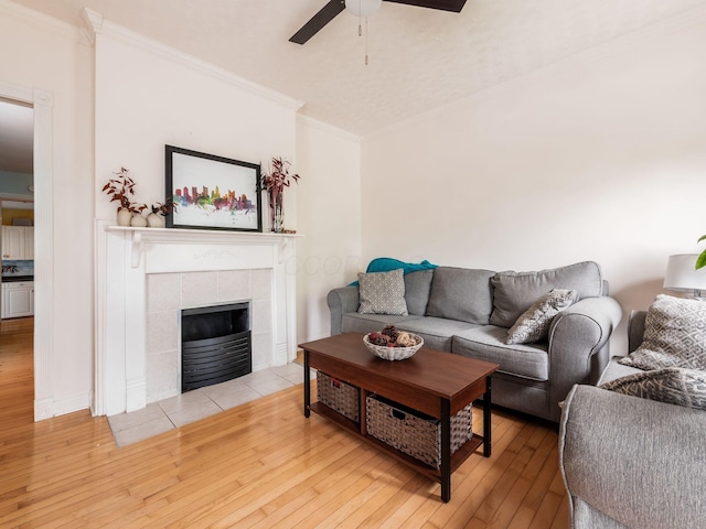 living room with ceiling fan, ornamental molding, hardwood / wood-style floors, and a tiled fireplace