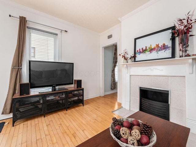 living area with baseboards, ornamental molding, a tiled fireplace, and hardwood / wood-style flooring