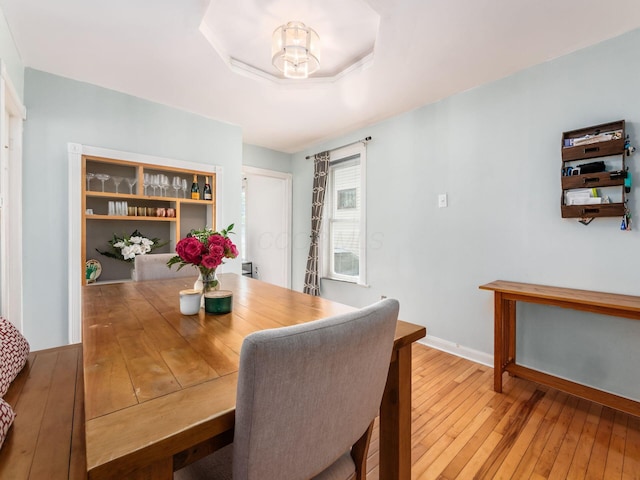 dining room featuring baseboards, a notable chandelier, a tray ceiling, and light wood-type flooring