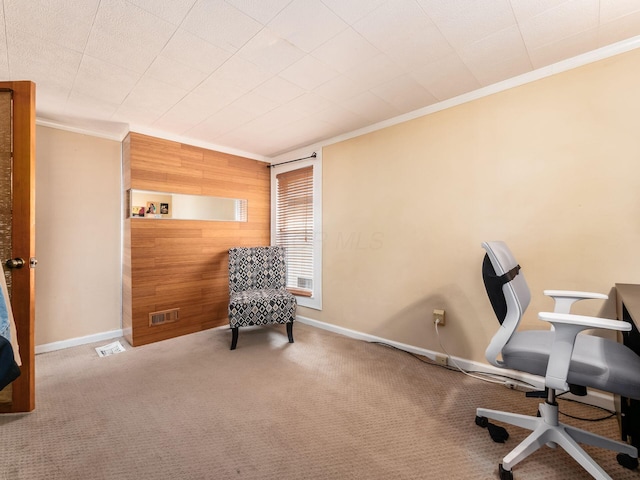 carpeted office space featuring visible vents, wood walls, baseboards, and ornamental molding