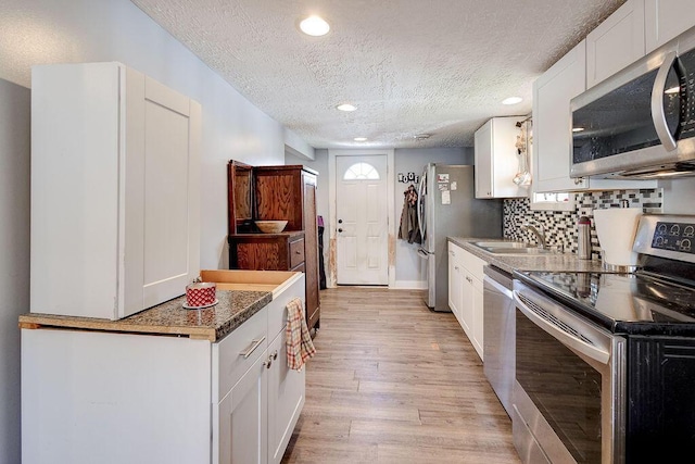 kitchen featuring a textured ceiling, light wood finished floors, a sink, white cabinetry, and appliances with stainless steel finishes
