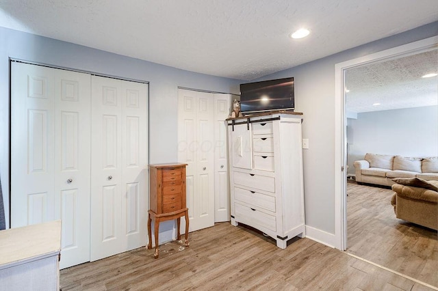 bedroom with baseboards, light wood-style floors, multiple closets, and a textured ceiling
