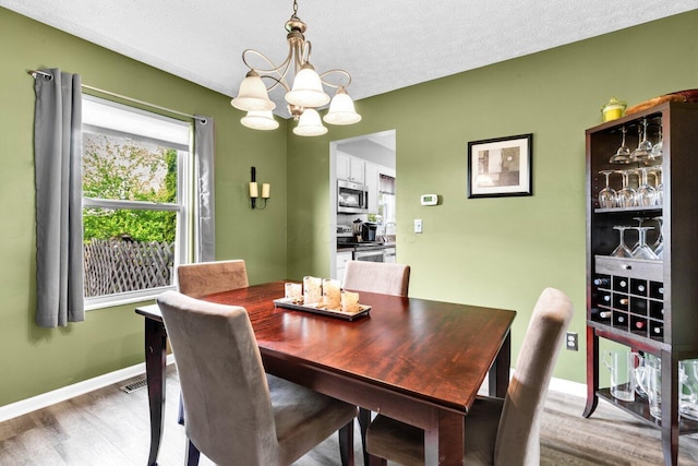dining space featuring an inviting chandelier, wood finished floors, a textured ceiling, visible vents, and baseboards