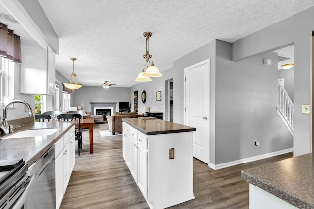kitchen featuring a sink, a fireplace, ceiling fan, stainless steel dishwasher, and dark countertops