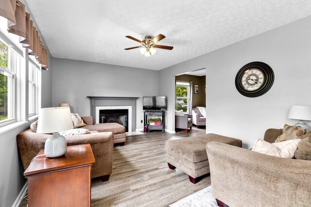 living area featuring a ceiling fan, a textured ceiling, baseboards, light wood finished floors, and a fireplace
