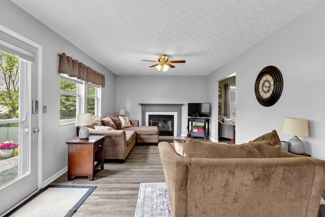 living room featuring a fireplace with flush hearth, a textured ceiling, baseboards, ceiling fan, and light wood-style floors