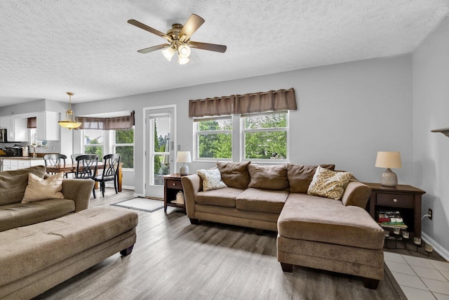 living area with ceiling fan, a textured ceiling, baseboards, and light wood-type flooring