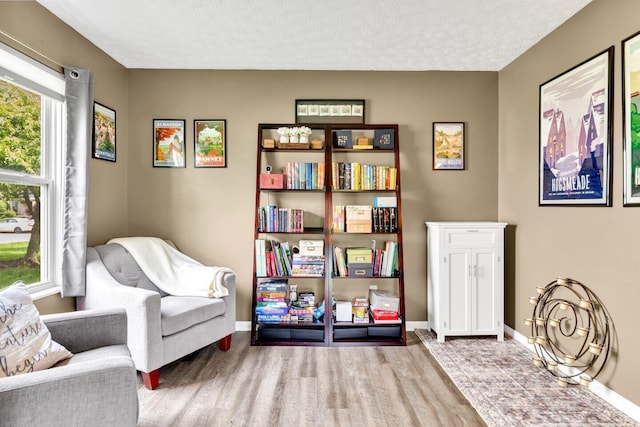 living area featuring a textured ceiling, wood finished floors, and baseboards